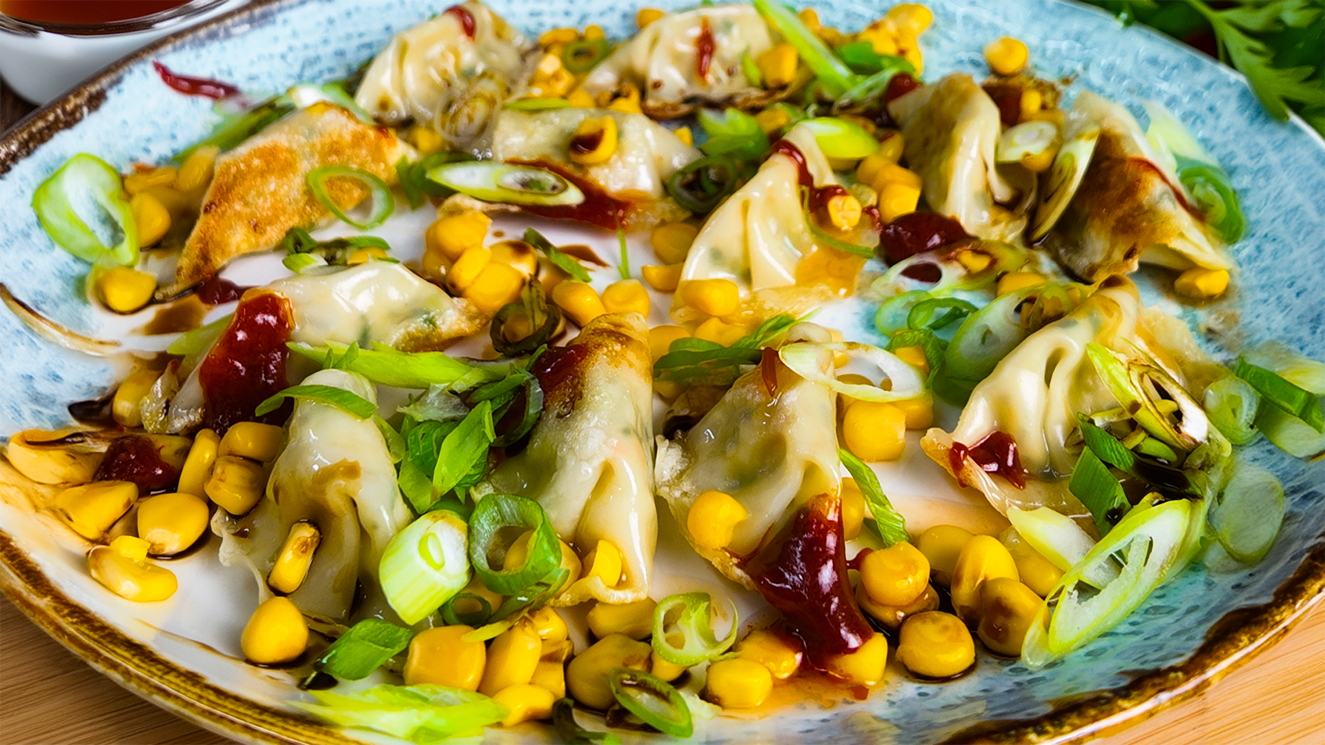 Gyozas auf einem Teller, garniert mit Mais, Hot Sauce und fein geschnittenen Frühlingszwiebeln, zubereitet mit dem FIVI Dampfgareinsatz aus Edelstahl.