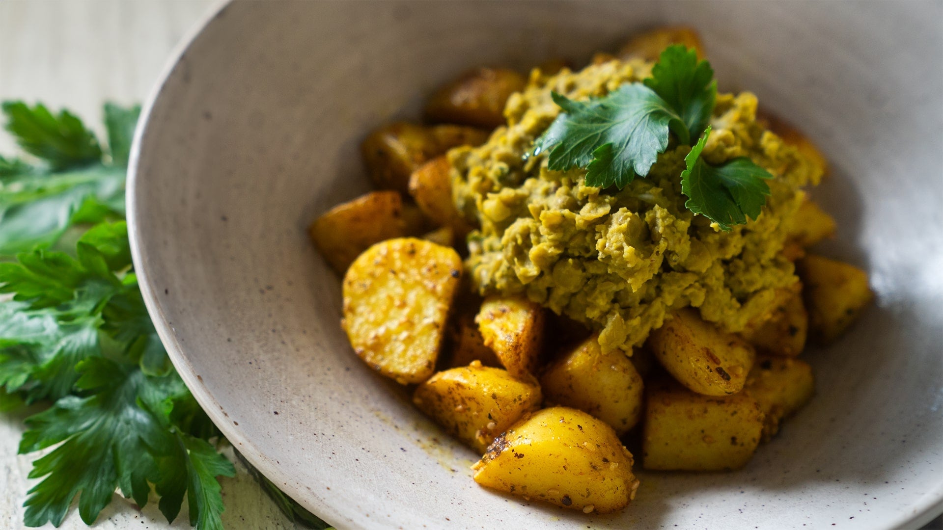 Kurkuma-Kartoffeln und Erbsen-Minze-Püree serviert in einer Schale, dekoriert mit frischen Kräutern, fotografiert vor einem grünen Hintergrund. Perfekt für ein gesundes und leckeres Gericht, zubereitet in der Schmorpfanne ALMAR von FIVI.