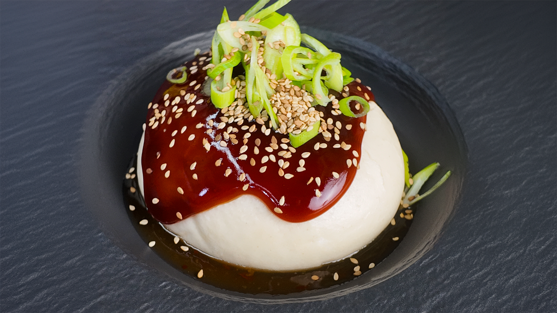 Leckere Bao Buns mit dunkler Austernsauce. Garniert mit Frühlingszwiebeln und Sesam auf dunklem Teller.