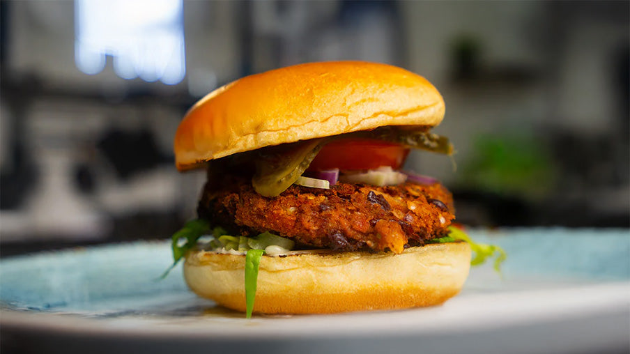 Veganer Burger mit Bohnen-Patty vor verschwommenen Hintergrund in einer Küche.