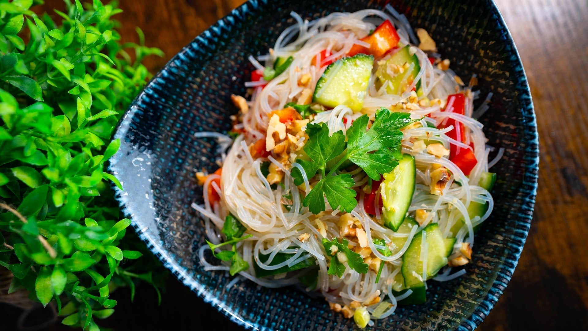 Asiatischer Glasnudelsalat mit knackiger Gurke, roter Paprika und gehackten Nüssen, serviert in einer schwarzen Schale – leicht, gesund und aromatisch.