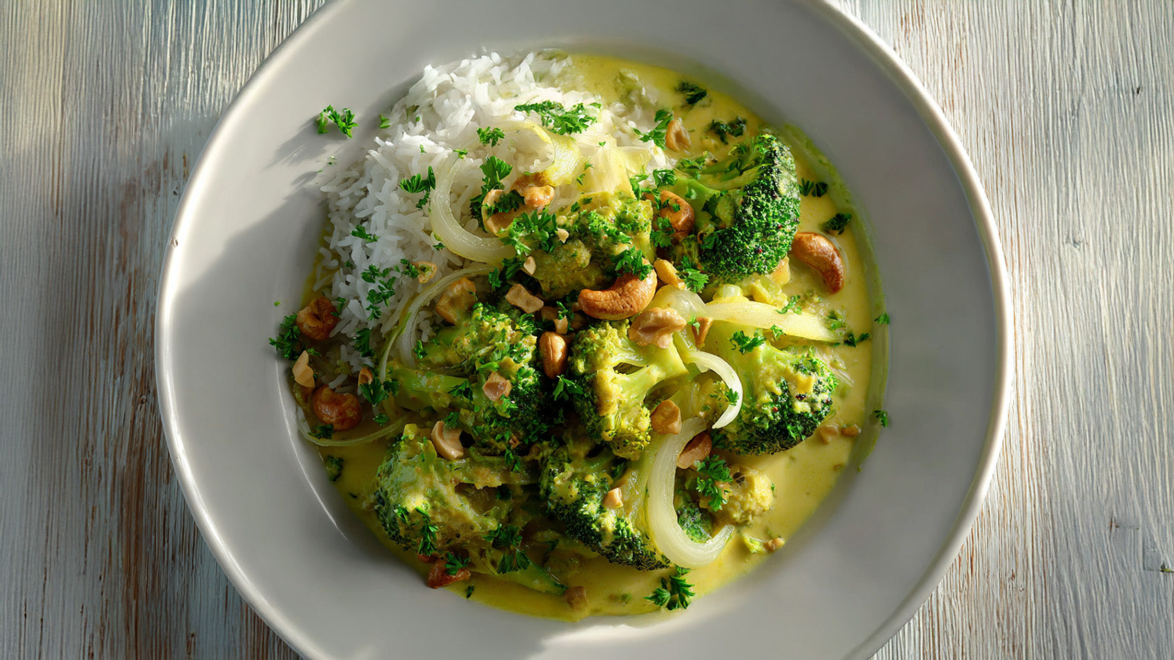 Brokkoli-Lauch-Curry mit Basmati-Reis in einer weißen Schale, cremige gelbe Currysauce, Brokkoli, Lauch und Cashewkernen, garniert mit frischer Petersilie.