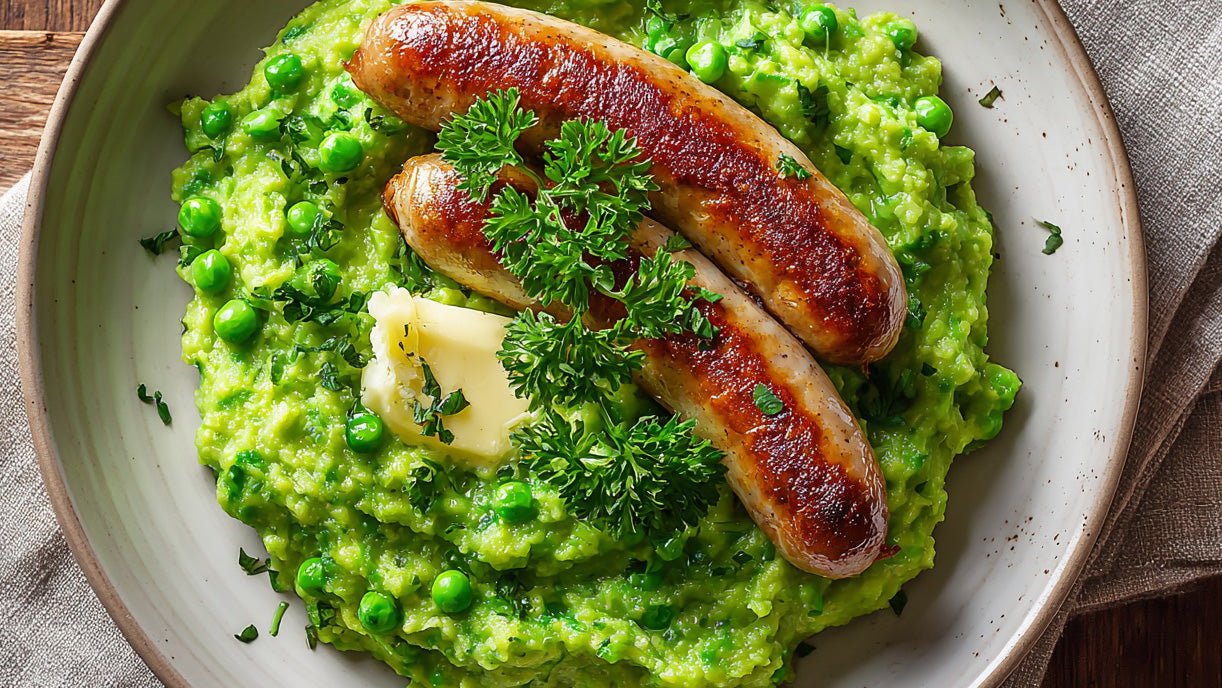 Erbsenstampf mit Bratwurst auf einem Teller, serviert mit Butterflocken und frischer Petersilie – cremiger Kartoffel-Erbsen-Stampf mit goldbraun gebratener Bratwurst.