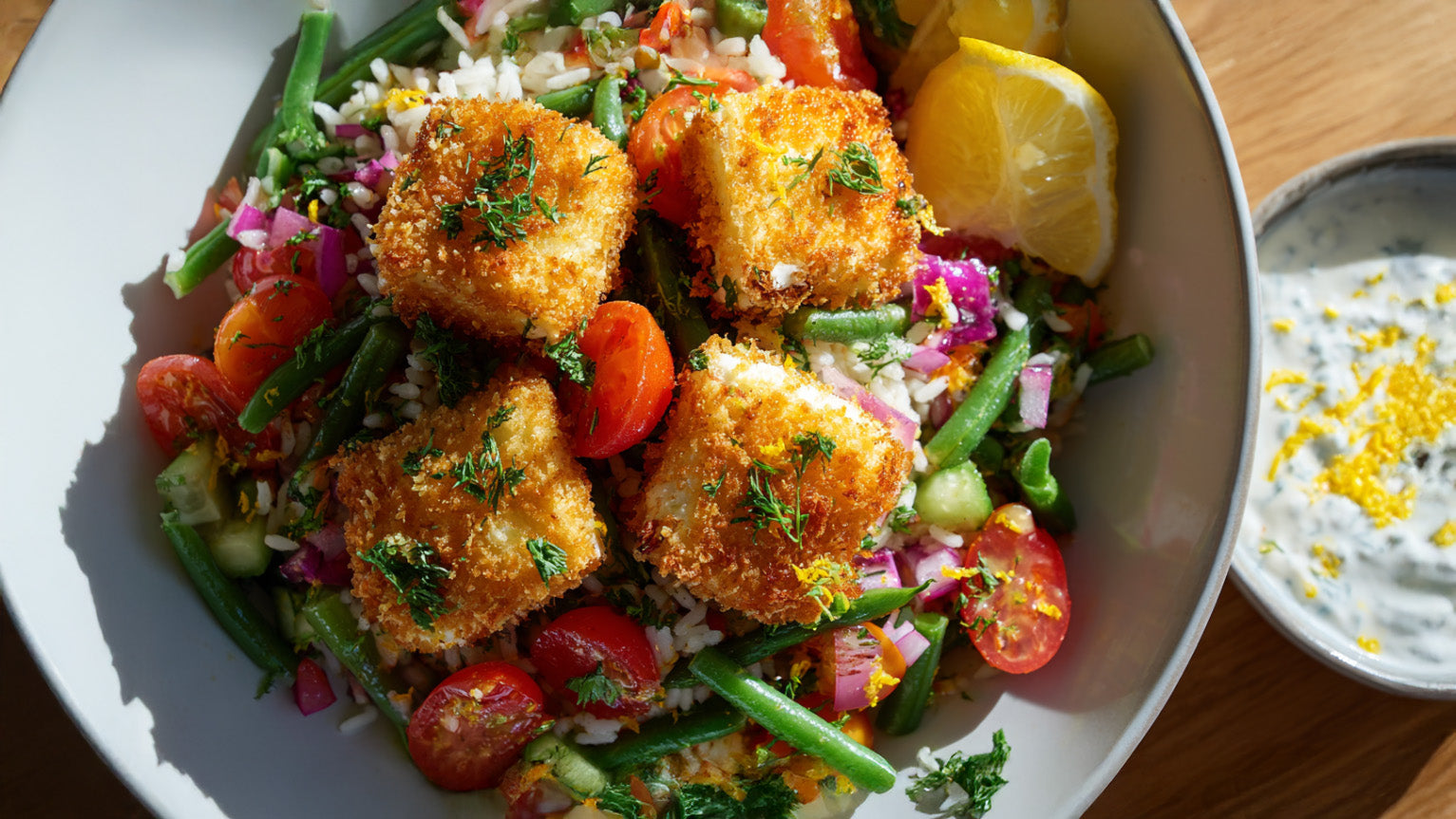 Knuspriger panierter Feta auf frischem Reissalat mit buntem Gemüse und cremigem Zitronen-Joghurt-Dip – ideal für leichte Sommergerichte.