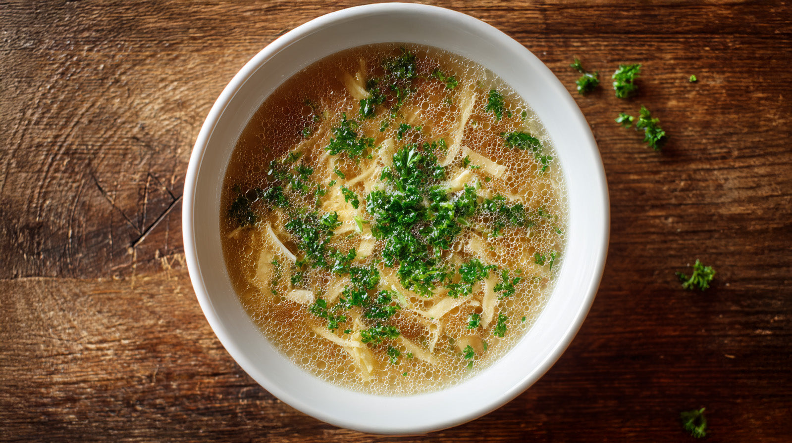 Flädlesuppe Rezept – hausgemachte Brühe mit feinen Pfannkuchenstreifen und frischer Petersilie in weißer Schüssel auf rustikalem Holztisch.