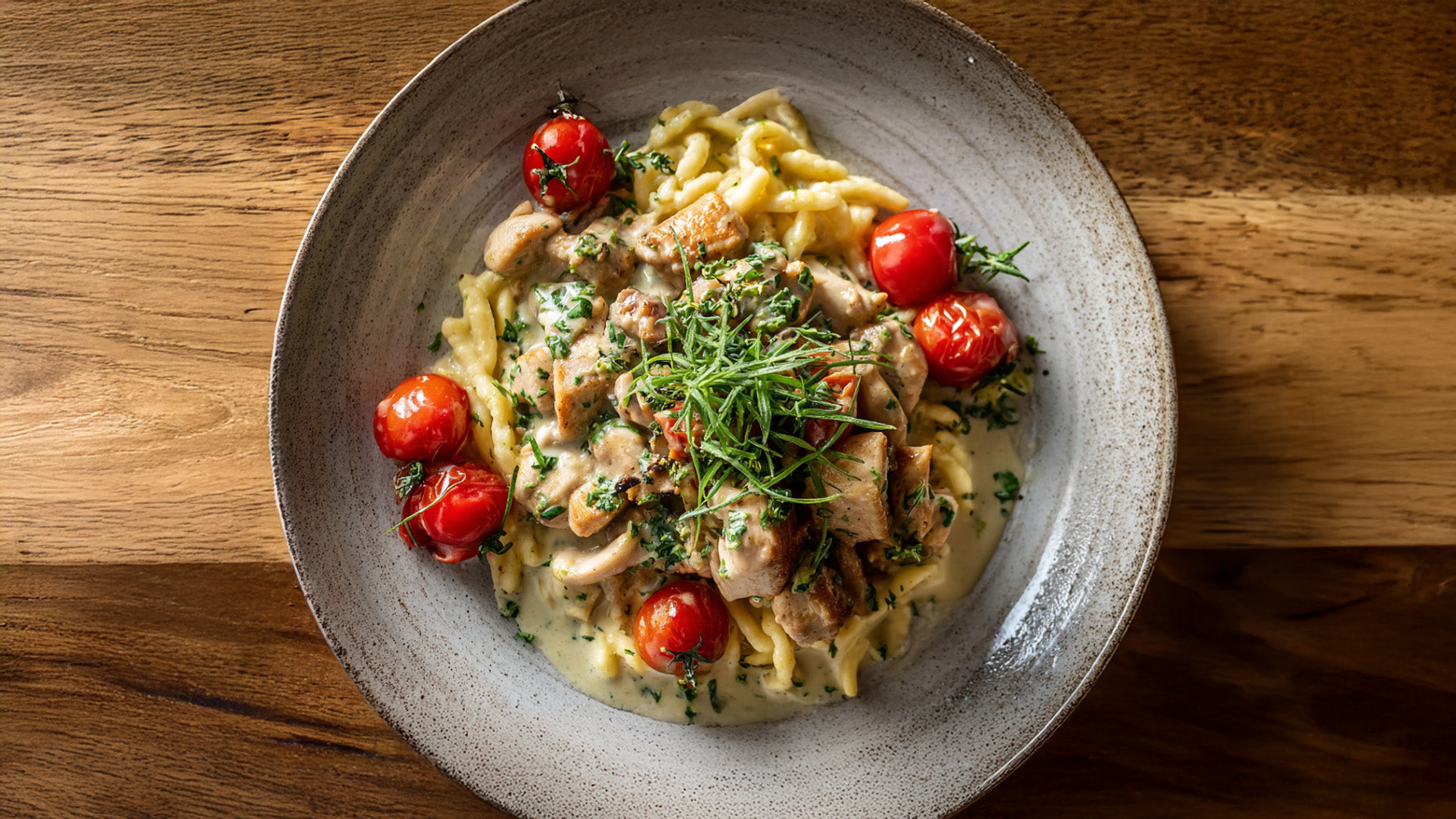 Hähnchen-Geschnetzeltes mit Spätzle in cremiger Estragon-Sahnesauce, serviert mit gebratenen Kirschtomaten auf rustikalem Teller