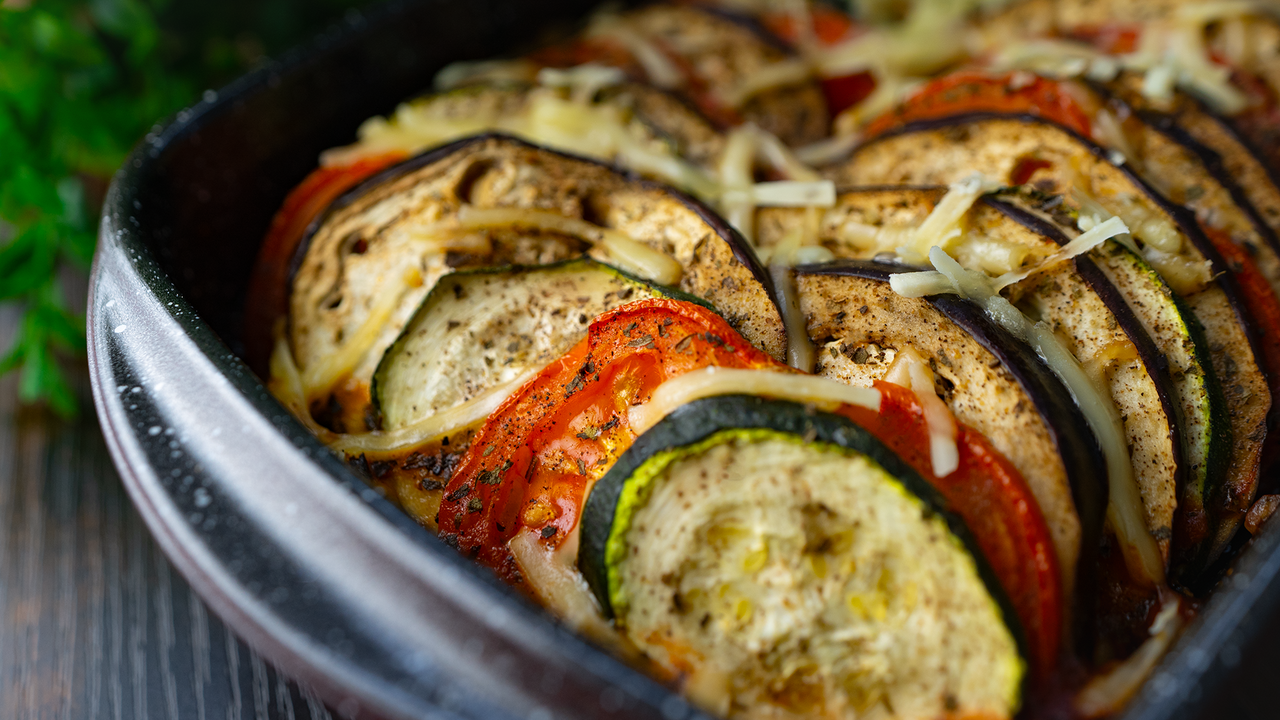 Ratatouille Rezept mit geschichteten Zucchini-, Auberginen- und Tomatenscheiben, vegan überbacken im Ofen – mediterranes Gemüsegericht in Nahaufnahme.