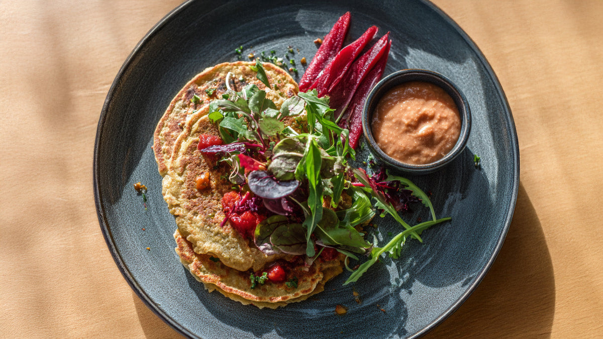 Linsen-Pancakes mit Feldsalat und Paprika-Walnuss-Dip auf dunklem Teller – gesunde, eiweißreiche Mahlzeit mit frischem Salat und Rote-Bete-Streifen.
