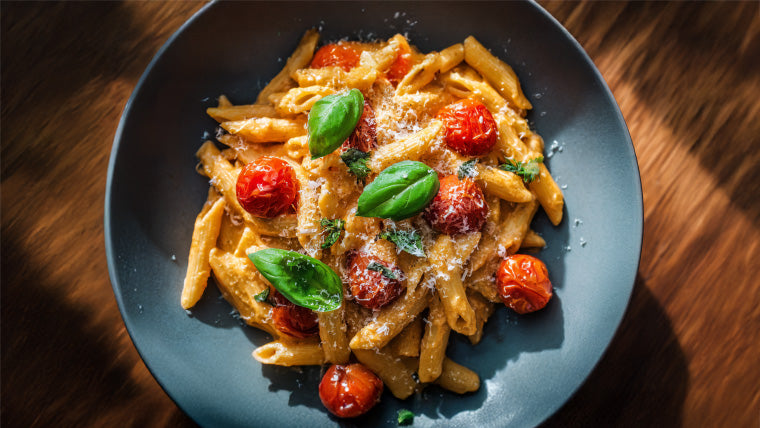 One Pot Pasta mit Tomaten und Basilikum in cremiger Sahnesauce, serviert mit Parmesan auf dunklem Teller