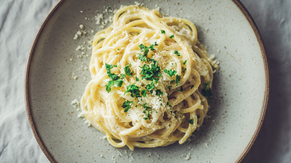 Draufsicht auf Pasta Alfredo mit cremiger Sauce, viel Parmesan und frischer Petersilie auf einem rustikalen Teller.