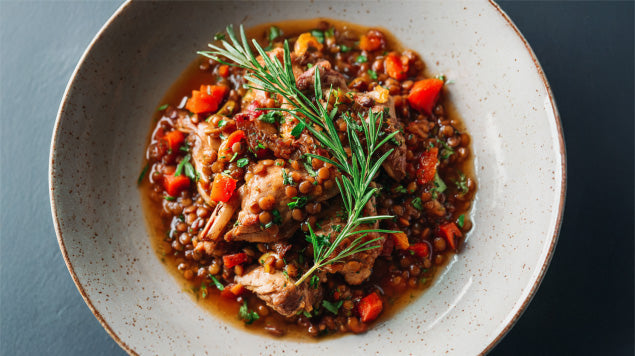 Kaninchen-Ragout mit roten Linsen, Möhren und Sellerie, angerichtet in einer hellen Schale, verfeinert mit frischen Kräutern