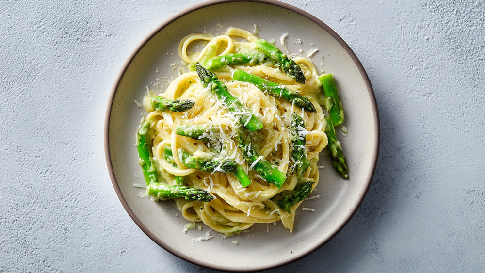 Spargel-Pasta cremig mit grünem Spargel und Parmesan auf hellem Teller angerichtet
