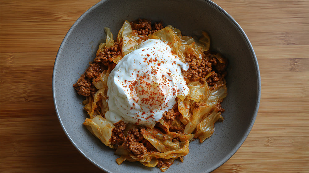 Rezept für Spitzkohl-Hackfleisch-Pfanne mit Joghurt-Topping und Paprikapulver in einer grauen Schüssel.