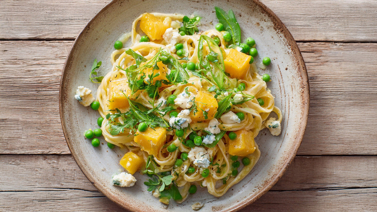 Cremige Pasta mit Steckrübe, Erbsen, Zuckerschoten und Ziegenfrischkäse, von oben fotografiert, serviert auf einem rustikalen Teller mit frischen Kräutern und Kresse, natürliche Beleuchtung auf Holztisch.