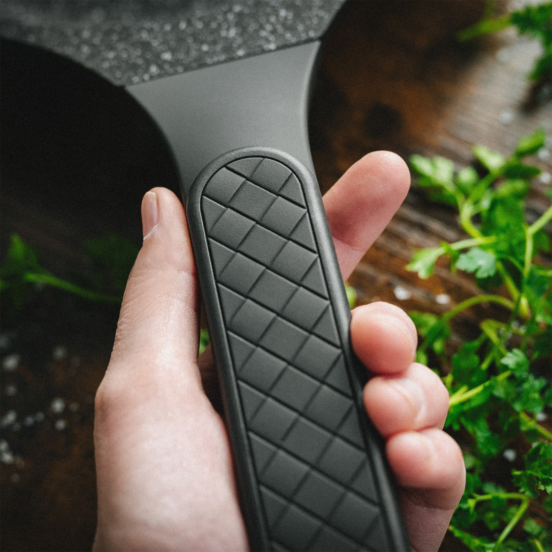 Nahaufnahme einer Hand, die den rutschfesten Griff der Alice Pfanne mit Karostruktur hält.