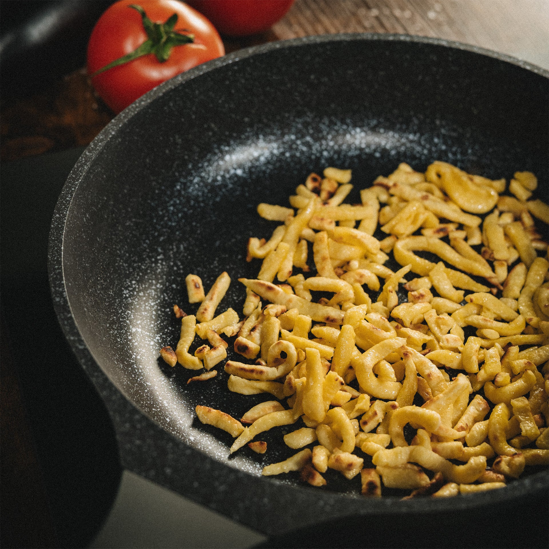 Goldbraun angebratene Spätzle in einer beschichteten Bratpfanne Alice mit frischen Tomaten.