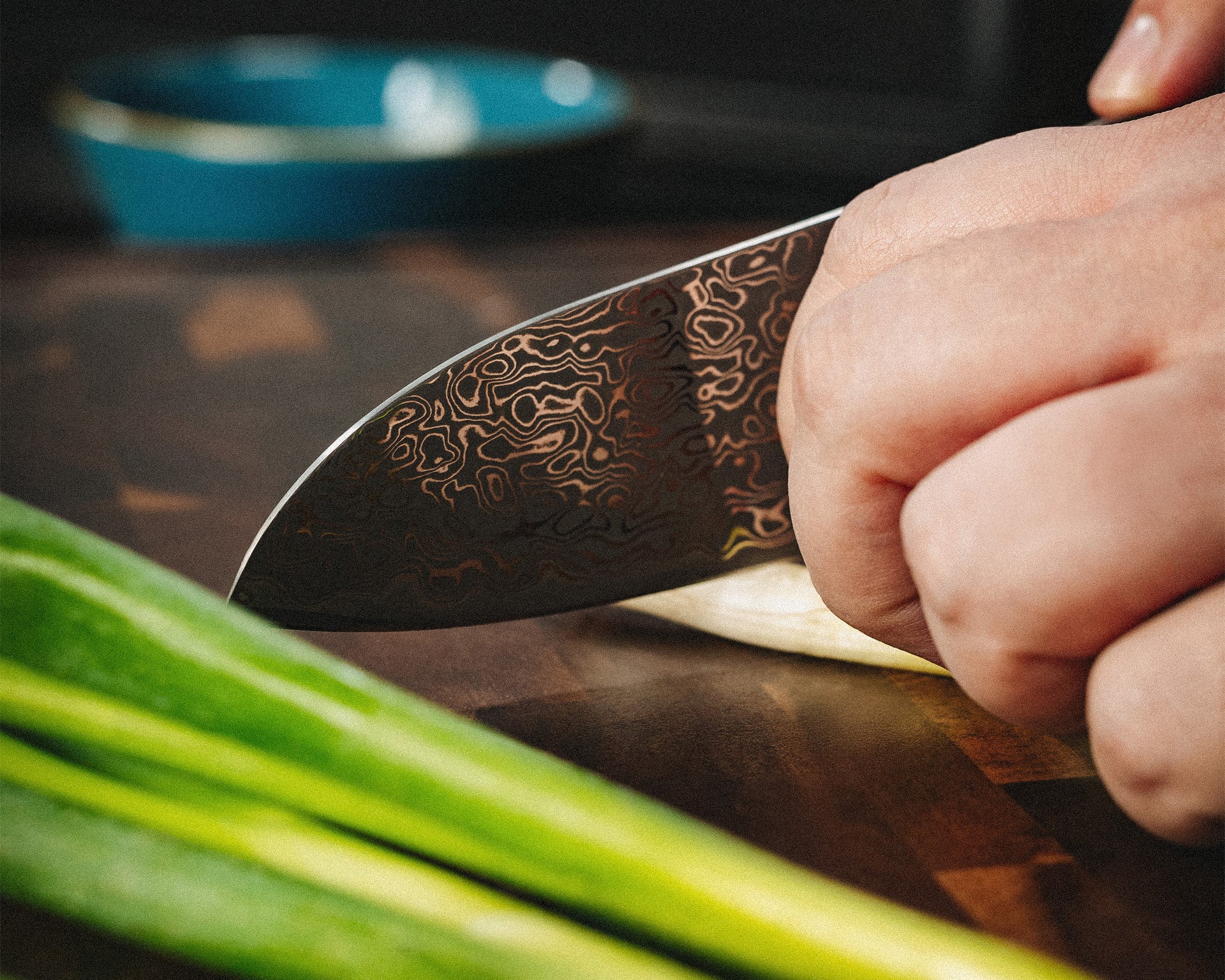 Nahaufnahme eines Damastmessers beim Schneiden von Frühlingszwiebeln auf einem Holzbrett.