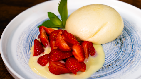 Fluffige Dampfnudel mit frischen Erdbeeren und Vanillesauce auf einem weißen Teller, dekoriert mit grünen Minzblättern