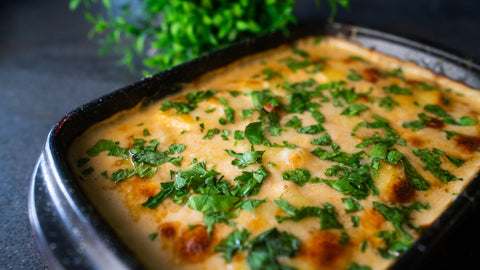 Cremiges Kartoffelgratin mit Parmesan goldbraun überbacken und mit Kräutern garniert. In dunkler STONELINE Auflaufform aus Borosilikatglas serviert vor dunklem Hintergrund.