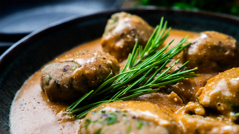 Semmelknödel mit cremiger Rahmsauce und frischem Rosmarin garniert, zubereitet in hochwertigem FIVI Kochgeschirr., serviert auf einem dunklen Teller