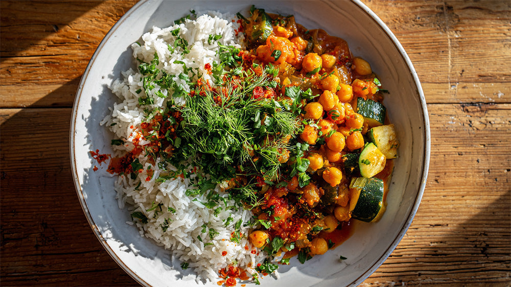 Draufsicht auf eine Kichererbsen-Zucchini-Pfanne mit Basmati-Reis, getoppt mit viel frischem Dill und Kräutern in einer Keramikschale auf Holzhintergrund.