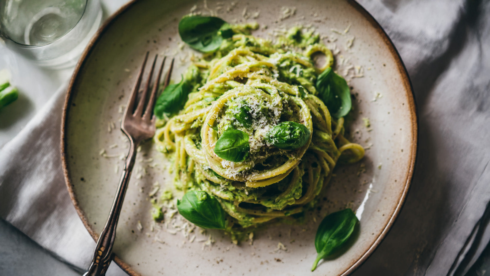Avocado Pasta mit cremiger Avocado-Sauce, frischem Basilikum und geriebenem Parmesan auf einem hellen Keramikteller