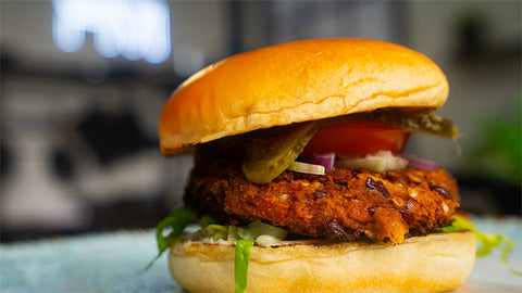 Veganer Burger mit Bohnen-Patty vor verschwommenen Hintergrund in einer Küche.