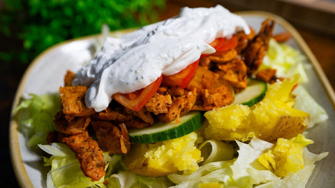 Veganes Rezept für Kartoffel-Döner mit Backkartoffel, veganem Gyros, frischem Gemüse und Knoblauch-Dip, angerichtet auf einem Teller mit Salat.