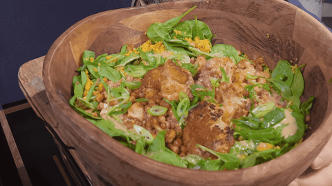 Blumenkohl Bowl mit Tahinsauce, geröstetem Blumenkohl, Kichererbsen und frischem Blattspinat, angerichtet in einer Holzschüssel, serviert auf Couscous mit FIVI Honey Hot Sauce.