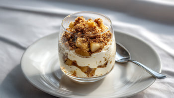 Bratapfel-Dessert im Glas mit cremiger Cheesecake-Schicht und zimtigen Apfelstücken auf einem weißen Teller.