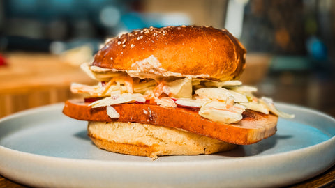 Leberkäs-Burger im Laugenbrötchen mit cremigem Coleslaw, serviert auf einem rustikalen Teller mit einer Schale Senf-Dip – bayerisches Streetfood mit herzhaftem Geschmack.