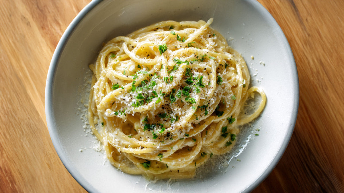 Garlic Noodles mit Parmesan und frischer Petersilie in einer grauen Schüssel auf Holztisch
