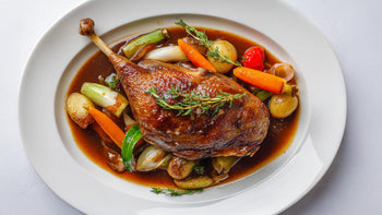 Gänsekeule Grundrezept auf aromatischem Schmorgemüse mit dunkler Sauce und frischem Thymian auf weißem Teller.