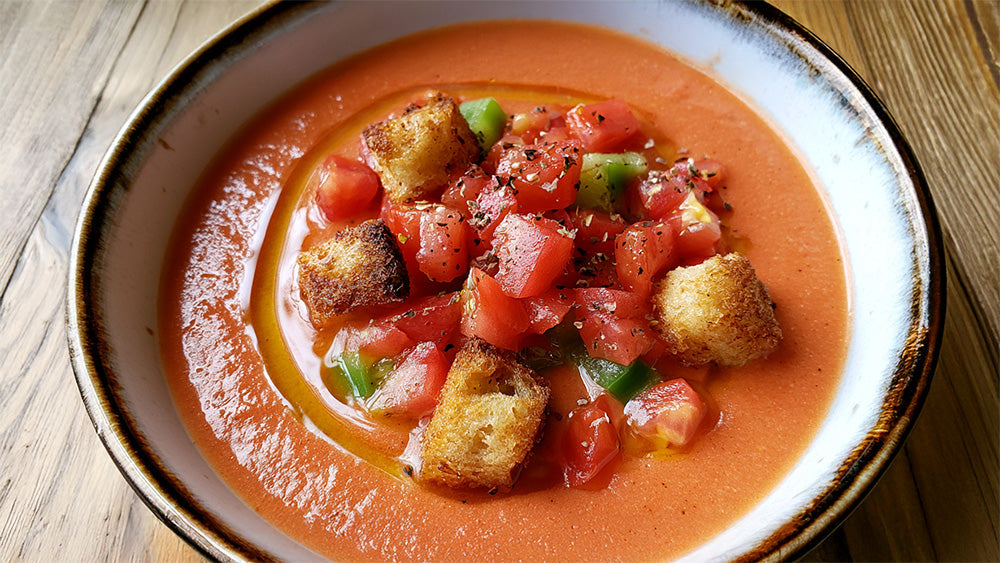 Schrägansicht einer Schale Gazpacho mit Tomatenwürfeln und Croutons.