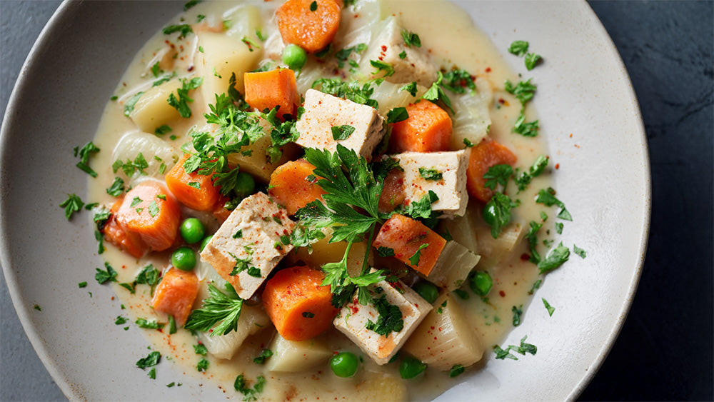 Cremiger Gemüseeintopf mit Tofu, Karotten, Kartoffeln und Erbsen, garniert mit frischer Petersilie auf einem Teller.