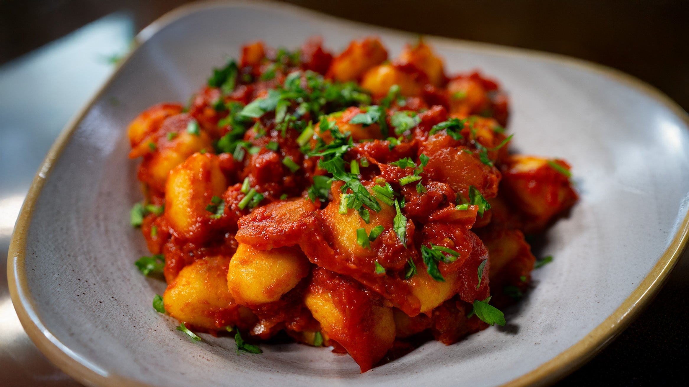 Nahaufnahme von Gnocchi in einer scharfen, stückigen Arrabiata-Tomatensauce, großzügig garniert mit frischer Petersilie, serviert in einem rustikalen grauen Teller mit organisch geformtem Rand.