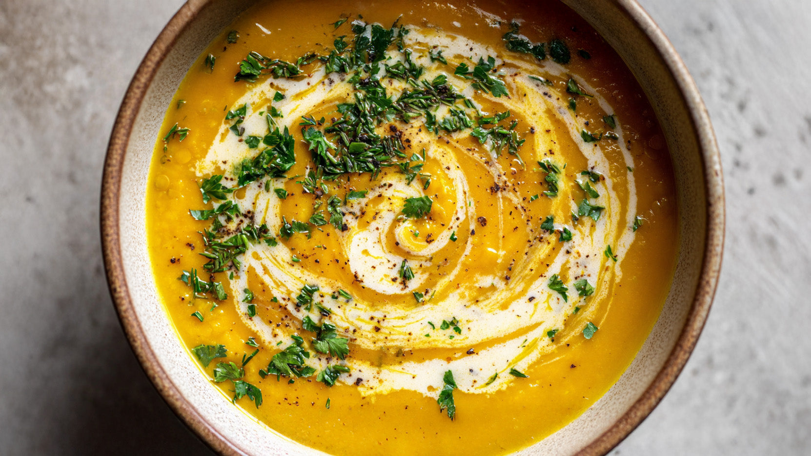 Goldene Linsensuppe mit Kokosmilch in einer Keramikschale, cremig püriert und mit Kokosmilch-Swirl, frischen Kräutern sowie schwarzem Pfeffer garniert.