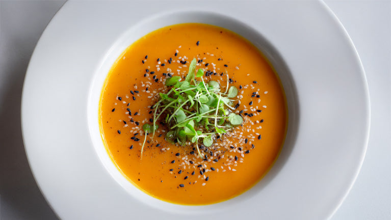 Karottensuppe mit Sesam und frischer Kresse in weißem Teller, cremig und leuchtend orange angerichtet