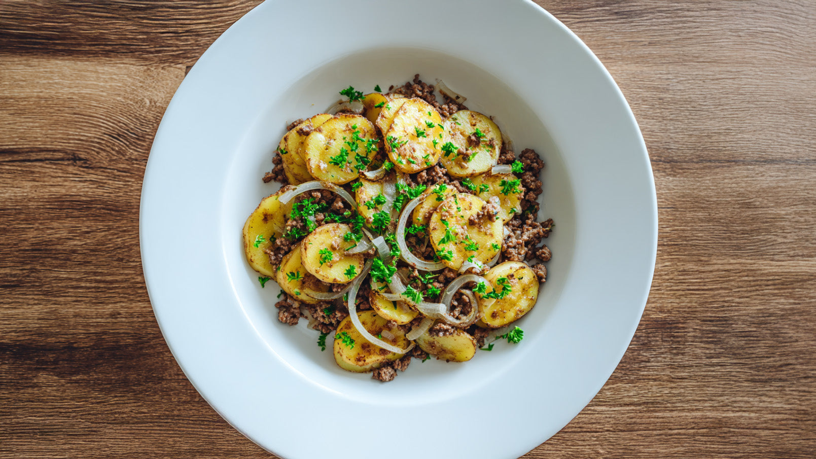 Kartoffel Hack Pfanne mit knusprig gebratenen Kartoffelscheiben, Hackfleisch und frischer Petersilie in weißer Schale