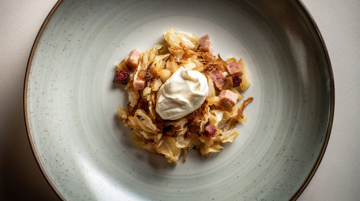 Weißkohl-Apfel-Pfanne mit Kasseler auf Teller – angerichtetes Kohl-Apfel-Gericht mit Kasselerwürfeln und Schmand als festliche Vorspeise.