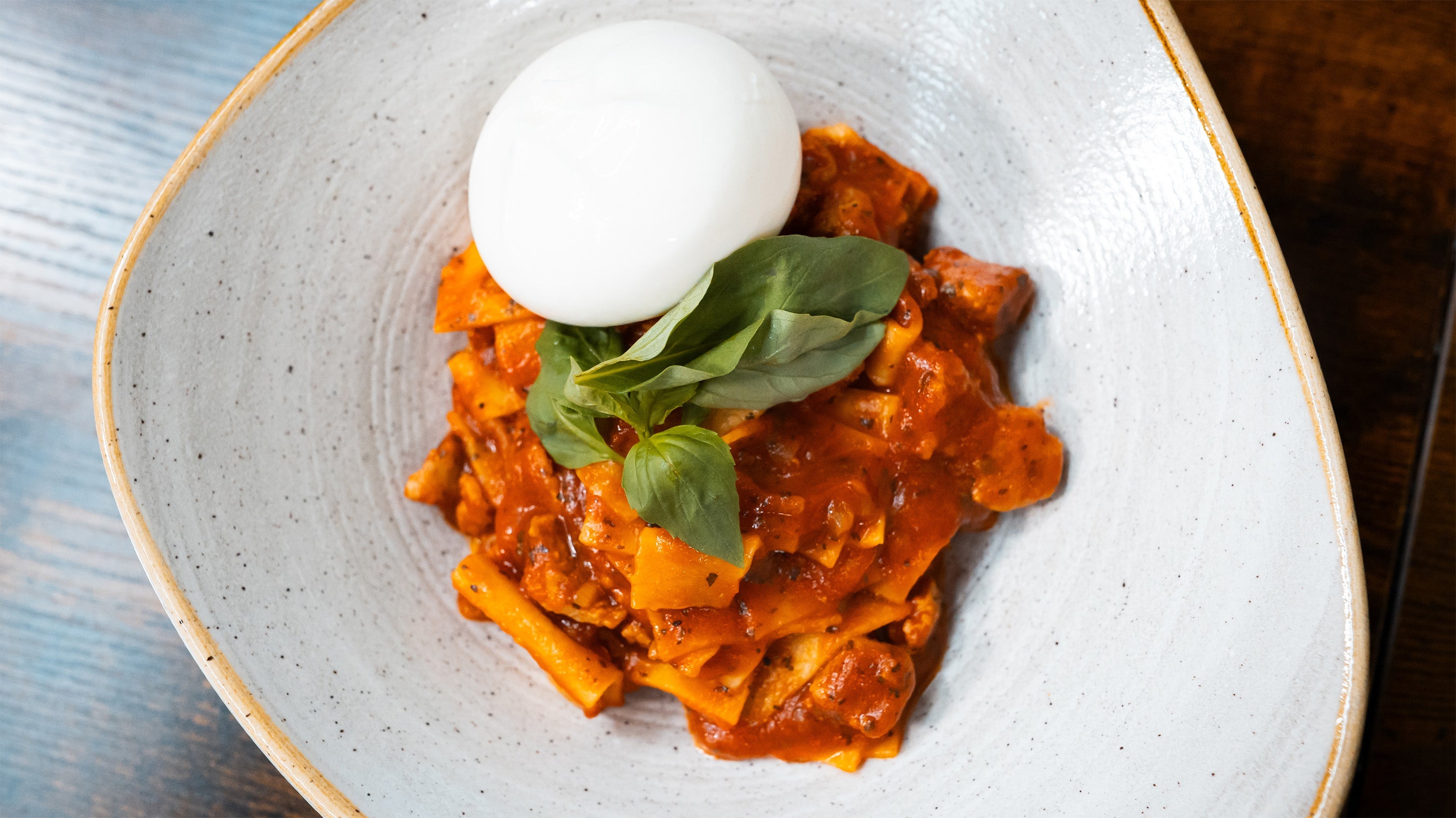 Servierte One Pot Lasagne in einer hellen Schüssel, garniert mit einer ganzen Burrata-Kugel und frischem Basilikum in der Draufsicht.