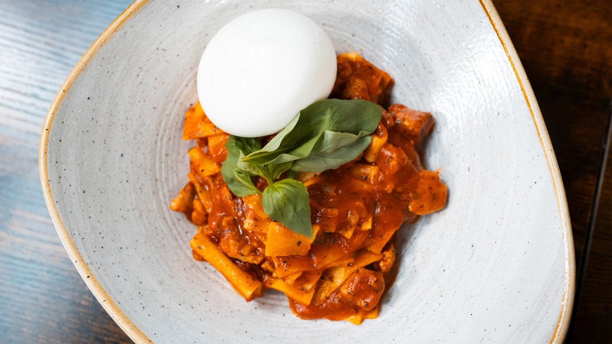 Servierte One Pot Lasagne in einer hellen Schüssel, garniert mit einer ganzen Burrata-Kugel und frischem Basilikum in der Draufsicht.