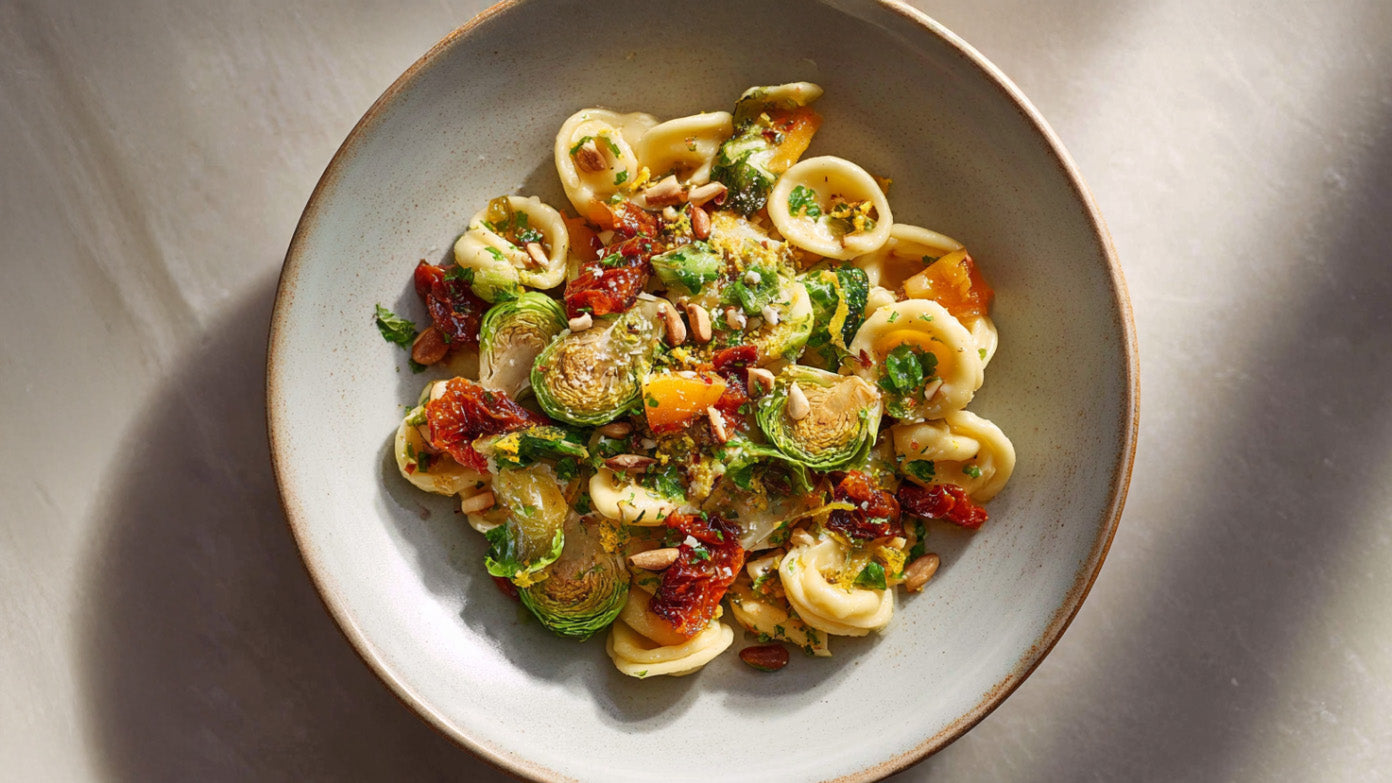 Orecchiette mit Rosenkohl in Schüssel, kombiniert mit getrockneten Tomaten, Aprikosen und gerösteten Pinienkernen, mediterran angerichtet.