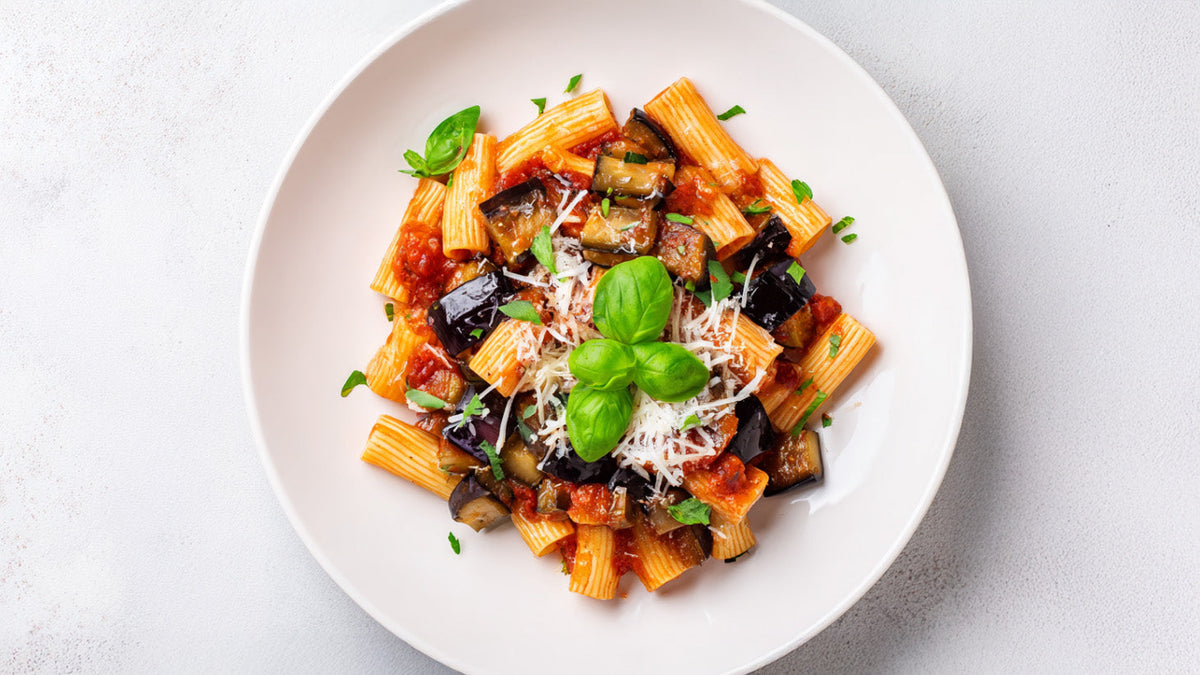 Pasta alla Norma mit Auberginen und Rigatoni in fruchtiger Tomatensauce, angerichtet auf weißem Teller, verfeinert mit Basilikum und frisch geriebenem Käse