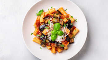 Pasta alla Norma mit Auberginen und Rigatoni in fruchtiger Tomatensauce, angerichtet auf weißem Teller, verfeinert mit Basilikum und frisch geriebenem Käse