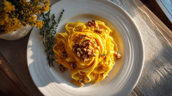 Bandnudeln mit Butternut-Kürbis auf weißem Teller, garniert mit Walnüssen und frischem Thymian – cremige Kürbis-Pasta in warmem Herbstlicht.