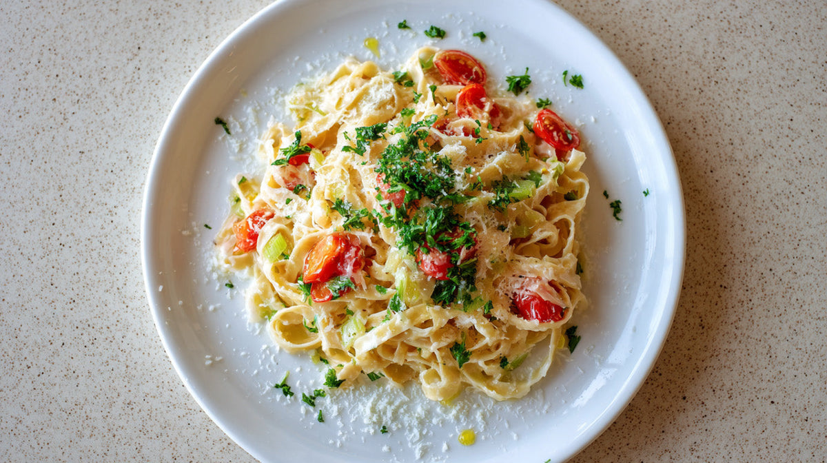 Pasta mit Lauch auf weißem Teller mit cremiger Sauce, Kirschtomaten, frisch geriebenem Pecorino und Petersilie, von oben fotografiert
