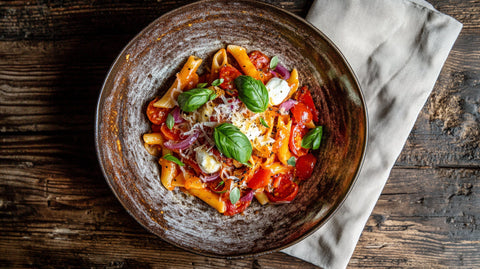 Pasta Mediterrana mit Kirschtomaten, Spitzpaprika, Mozzarella und frischem Basilikum auf einem rustikalen Teller – mediterranes Pastagericht voller Aromen.