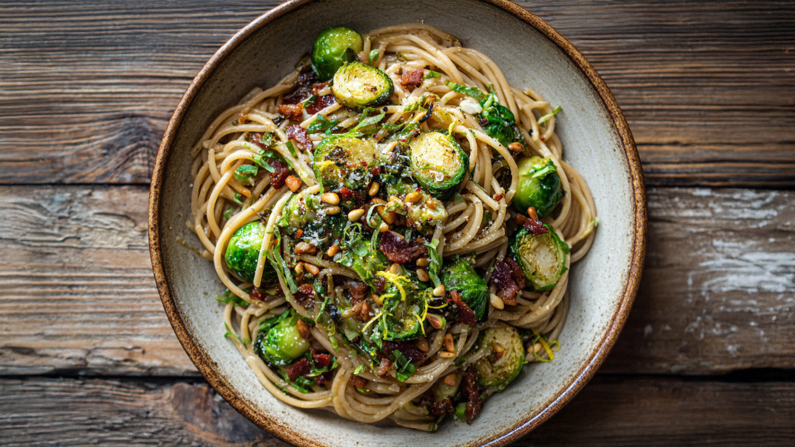 Pasta mit Rosenkohl & Speck – Vollkorn-Spaghetti mit knusprigem Speck, gerösteten Pinienkernen und frischem Zitronenabrieb auf rustikalem Holztisch.
