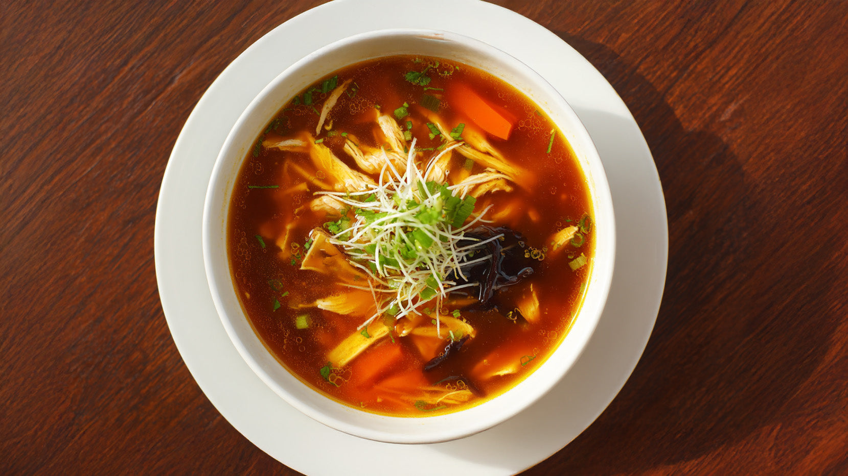 Pekingsuppe mit Hähnchen, Karotten, Mu-Err-Pilzen und Frühlingszwiebeln in weißer Schale von oben fotografiert